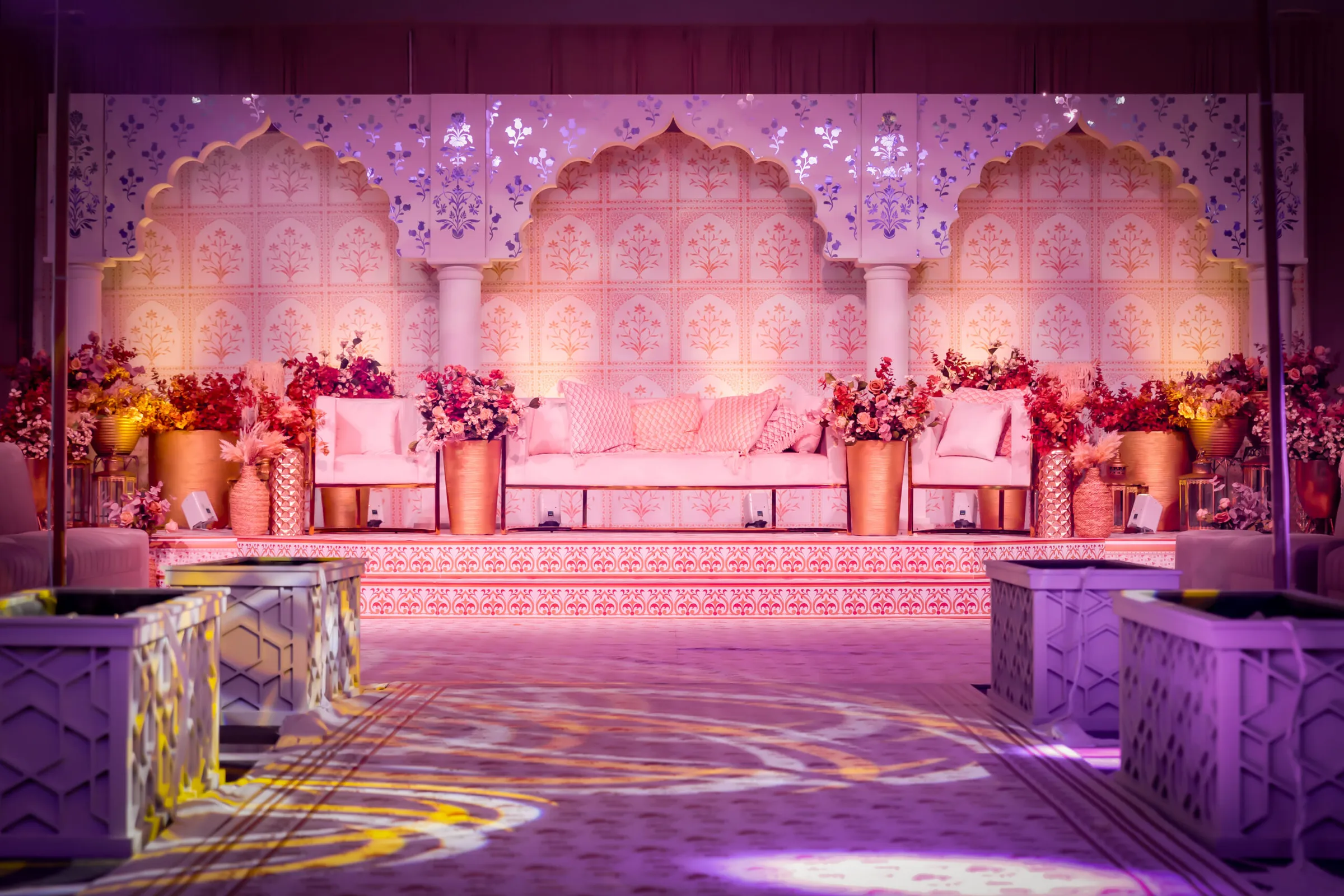 The Zari stage: carved jali arches lit in pink, with gold planters and red flowers